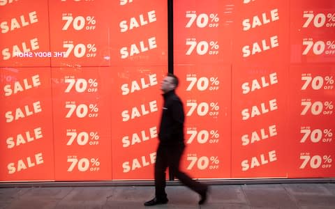 People out shopping on Oxford Street walk past large scale January sale signs