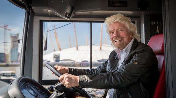 Branson sits in the driver's seat of a coach bus.
