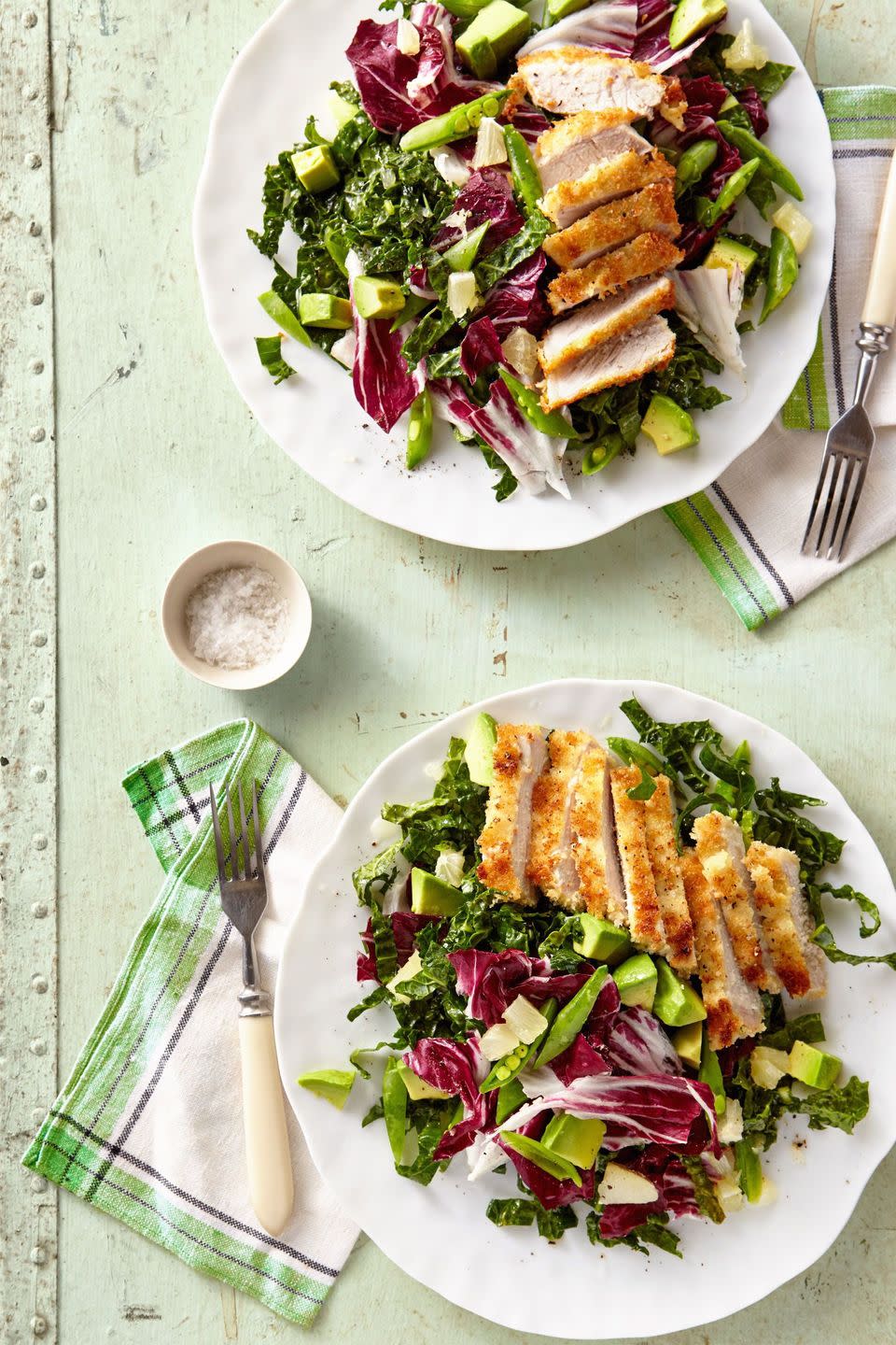 breaded pork cutlet with avocado kale salad on a white plate with a fork