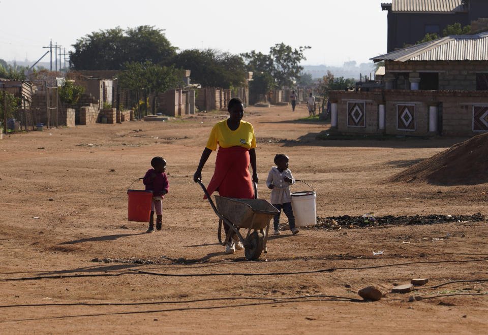 A woman, with two children, makes her way to a water tank to collect water in the Hammanskraal township, Pretoria, South Africa, Wednesday, May 22, 2024. Hammanskraal’s problems are a snapshot of the issues affecting millions and driving a mood of discontent in South Africa that might force its biggest political change in 30 years in next week’s national election. (AP Photo/Denis Farrell)