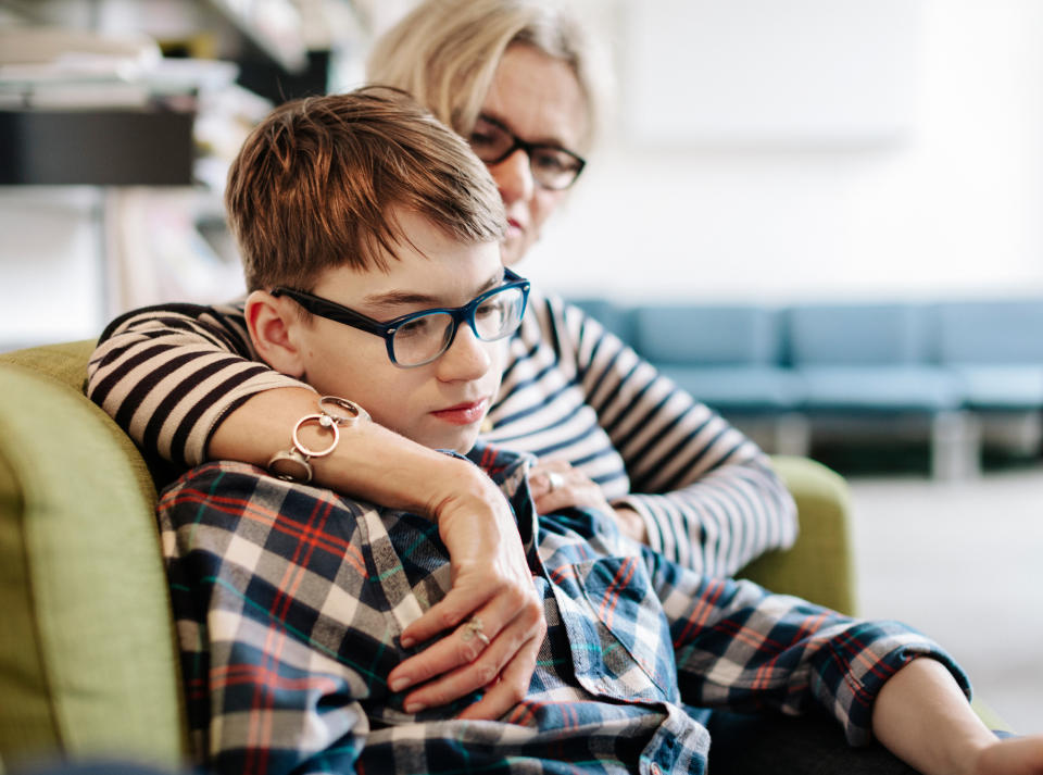 Adult cradles a child on a green sofa. Both are wearing glasses. The adult is in a striped top, and the child is in a plaid shirt. Warm, comforting atmosphere