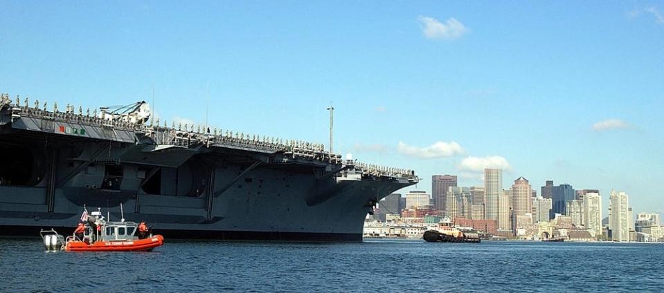 a 25-foot Defender Class boat and USS John F. Kennedy in the port of Boston