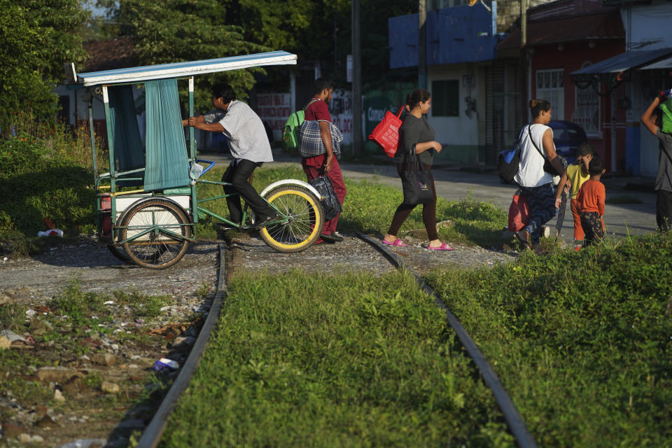 Migrants walk across the train tracks past a local bicycle taxi driver in Huixtla, Chiapas state, Mexico, early Tuesday, Oct. 26, 2021, as the migrants' group uses the day to rest during their ongoing trek by foot toward the U.S. (AP Photo/Marco Ugarte)