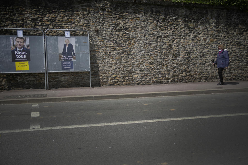 FILE - A woman walks past campaign posters of French President Emmanuel Macron and candidate for the re-election, left, and far-right presidential candidate Marine Le Pen in Ville d'Avray, outside Paris, France, April 20, 2022. Disgruntled left-wing voters whose candidates were knocked out in the first round of France's election are the wild cards in the winner-takes-all runoff on Sunday April 24, 2022. How they vote — or don’t vote — will in large part determine whether incumbent Emmanuel Macron gets a second five-year term or cedes the presidential Elysee Palace to far-right nationalist Marine Le Pen. (AP Photo/Christophe Ena, File)