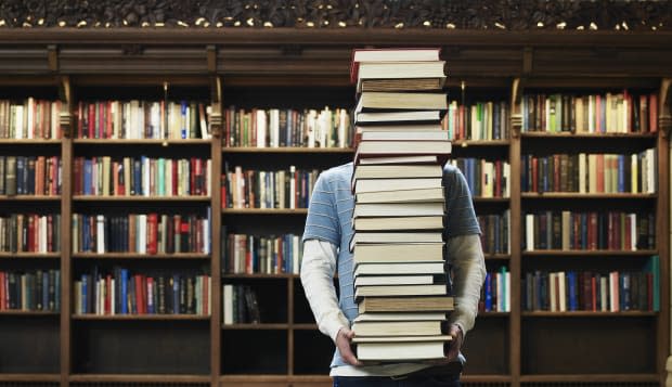 Young man carrying stack of books in university library