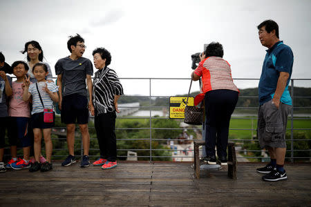 A woman looks toward the north as a family poses for photographs at an observation platform near the demilitarized zone separating the two Koreas in Paju, South Korea, August 14, 2017. REUTERS/Kim Hong-Ji