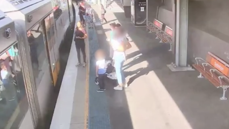 The boy stands next to his mother and a pram on the platform at Sydenham station as the train pulls up. 