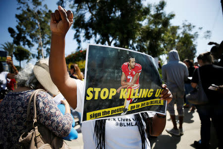 A protester demonstrates and holds a sign with Colin Kaepernick on it in support of NFL players who "take a knee" before kickoff and during the National Anthem protesting police violence while she sings the "Black National Anthem" outside the StubHub Center where the Los Angeles Chargers are playing the Philadelphia Eagles in an NFL football game in Carson, California, U.S. October 1, 2017. REUTERS/Danny Moloshok