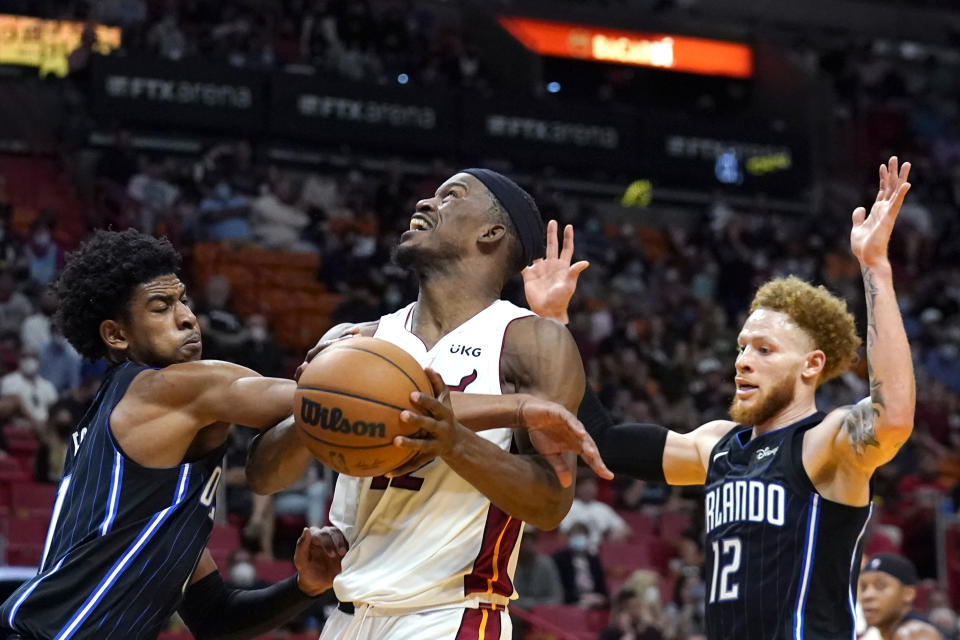 Miami Heat forward Jimmy Butler (22) goes to the basket as Orlando Magic forward Aleem Ford, left, and guard Hassani Gravett (12) defend during the first half of an NBA basketball game, Sunday, Dec. 26, 2021, in Miami. (AP Photo/Lynne Sladky)