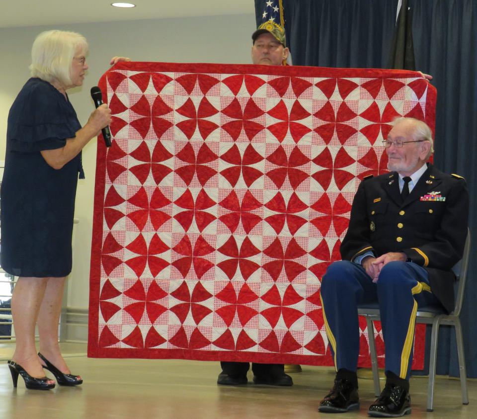 Lt. Col. Janssen receiving the “Quilt of Valor” from Joan Lane of the Rainbow Springs Quilts of Valor and President Charles Calhoun of the OTOW Veterans Club. From left: Joan Lane, Charles Calhoun standing behind the quilt, and Lt. Col. Arlo Janssen seated.