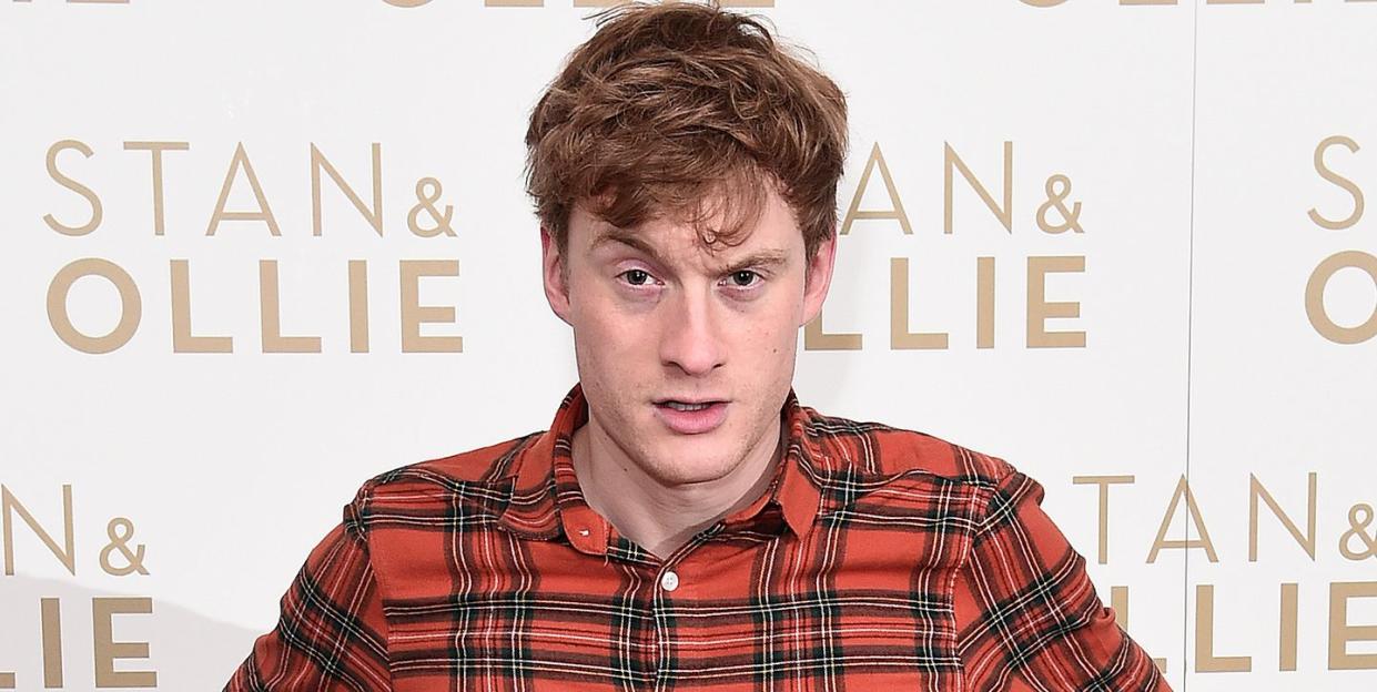 james acaster, a man stands with hands on hips wearing a red check shirt