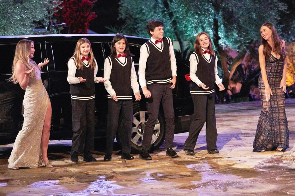 Rachel Recchia and Gabby Windey stand on opposite sides of a children's show choir as they sing in front of a limo in this still from the season 19 premiere of "The Bachelorette."