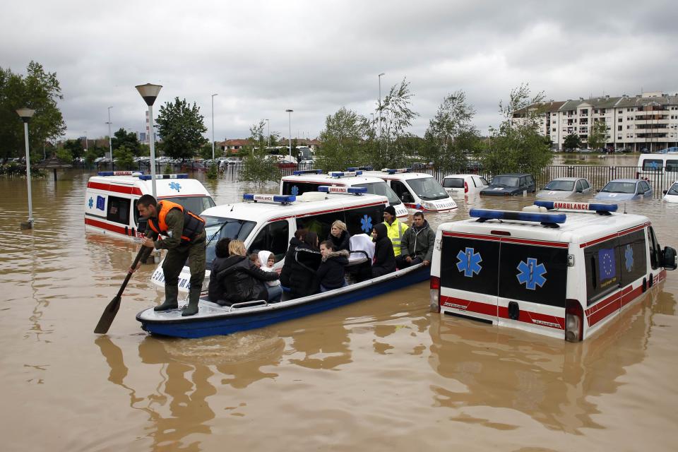 Serbian rows a boat past flooded ambulance vehicles in the flooded town of Obrenovac