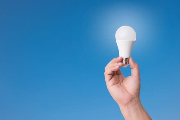 Hand holding an LED lightbulb in front of a blue background