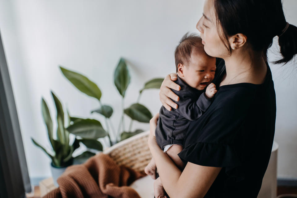 A loving young Asian mother carrying her newborn baby girl in arms, consoling and comforting her crying baby. Hunger and discomfort. Love and care. Motherhood and parenthood concept