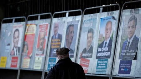 A man looks at campaign posters of the 11th candidates who run in the 2017 French presidential election in Enghien-les-Bains, near Paris, France April 19, 2017. REUTERS/Christian Hartmann - RTS12ZQ5