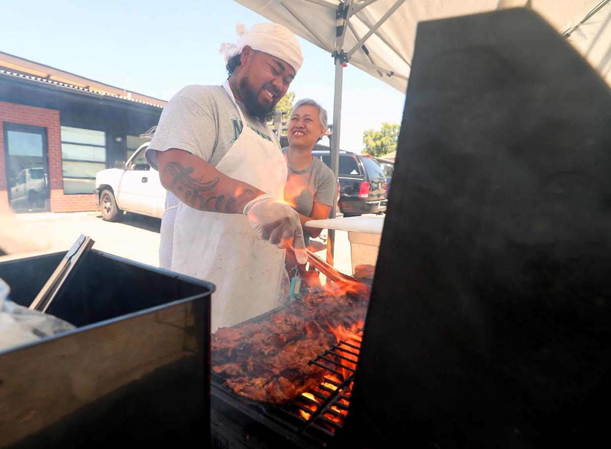 The Island Hut's Channa Tupai, right, smiles at her son Monk as he grills chicken for those living on the sidewalk of MLK Way in Bremerton on July 31.