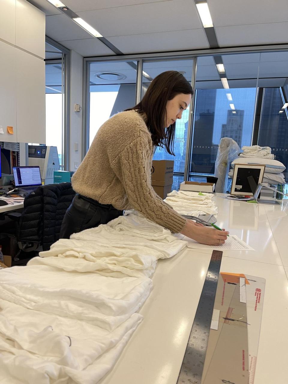 a woman touching one fabric sample from a row of different white sheet fabrics to evaluate softness and feel