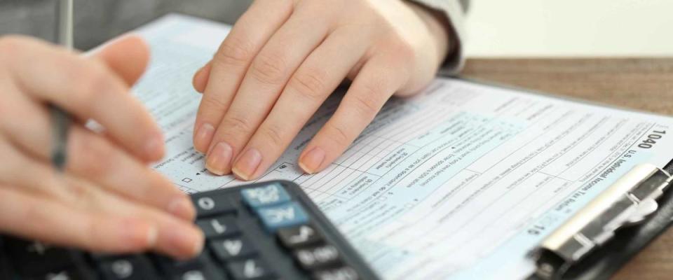 Female hand holding a pen and using calculator while filling in the individual income tax return, close up