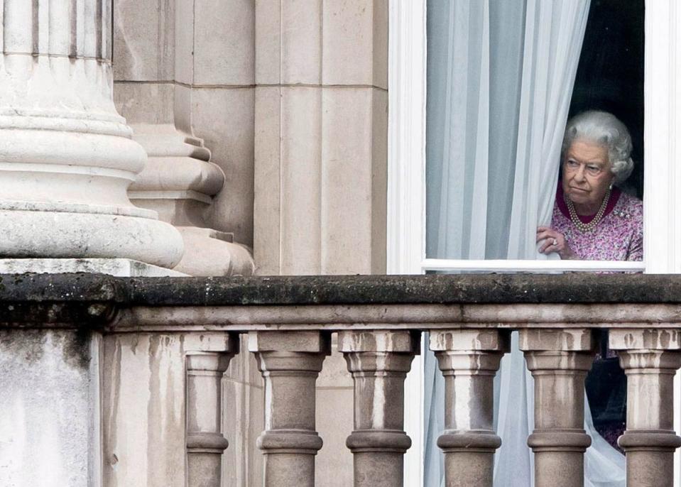 Queen Elizabeth II peers out a window from behind a curtain in Buckingham Palace (Tim Rooke/Shutterstock)