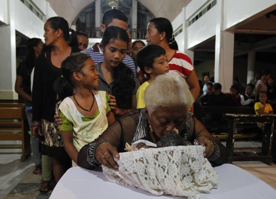 Victims of the onslaught of super typhoon Haiyan a month ago, wait in line to kiss a figurine of baby Jesus during a Christmas Eve mass at a Catholic church in San Joaquin town in Palo