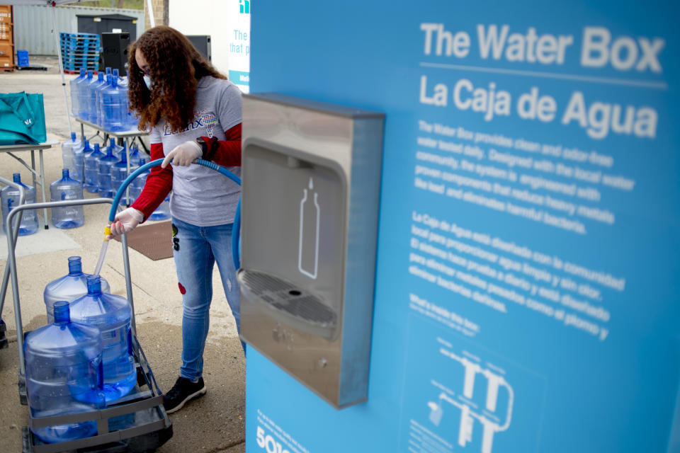 FILE - Volunteer Evelyn Cano, of Flint, helps fill five-gallon jugs for Flint residents using The Water Box on the eve of the seventh anniversary of the Flint water crisis during a water distribution on Saturday, April 24, 2021 at the Latinx Technology & Community Center in Flint, Mich. A second contractor says it has reached a $25 million settlement over its role in Flint's lead-contaminated water scandal. Boston-based Veolia North America said Thursday, Jan. 31, 2024, that the class-action litigation agreement includes payments of $1,500 for individual minors. (Jake May/The Flint Journal via AP, File)