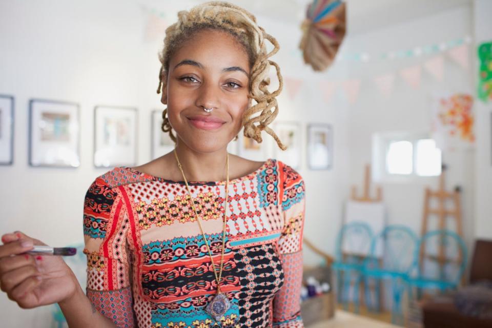 A warmly smiling woman holds a paintbrush