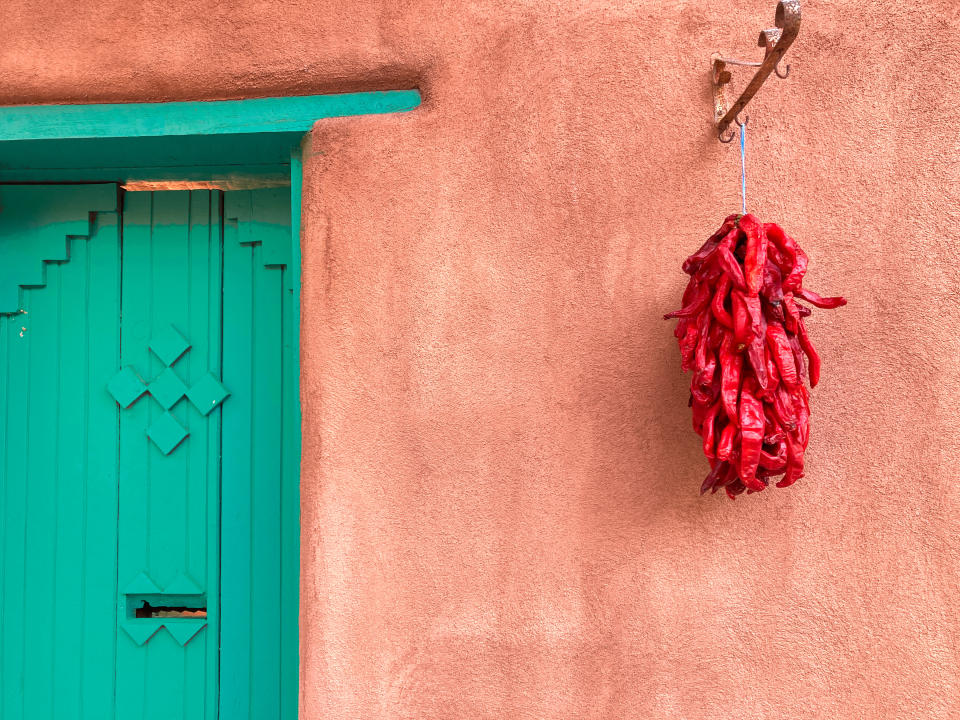 Dried red chiles hanging from a coral wall next to a green door