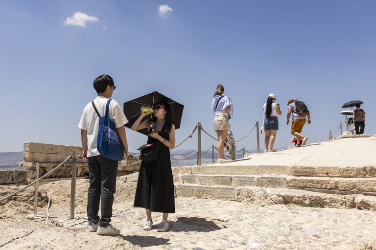 Los turistas caminan bajo sombrillas durante su visita a la Acrópolis de Atenas en plena ola de calor el 
18 de junio de 2024, Grecia