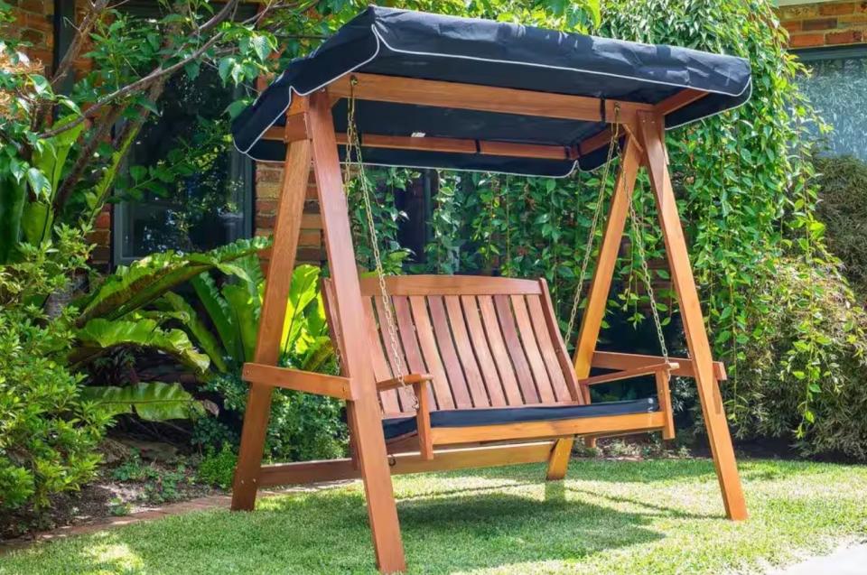 Swinging garden seat with a built-in black awning set up in a yard.