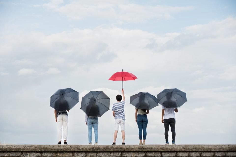 Five figures in a row, two holding black umbrellas on either side of one holding a red umbrella.