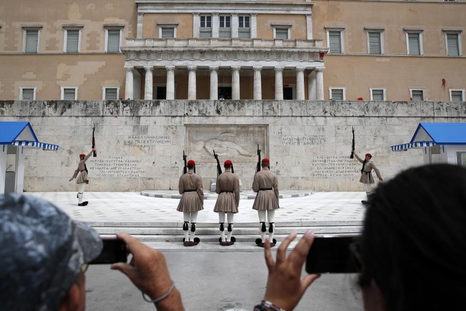 Red paint is seen on the wall of the Parliament building as Greek Presidential Guards, changing of the guard at the tomb of the unknown Soldier in Athens, Tuesday, May 21, 2019. A group of about 10 people threw red paint at parliament and set off a smoke bomb as Greece's Supreme Court is hearing an appeal against the denial of a temporary leave of absence from prison of a hunger striking extremist serving multiple life sentences for the killings of 11 people by the country's deadliest far-left group. (AP Photo/Thanassis Stavrakis)