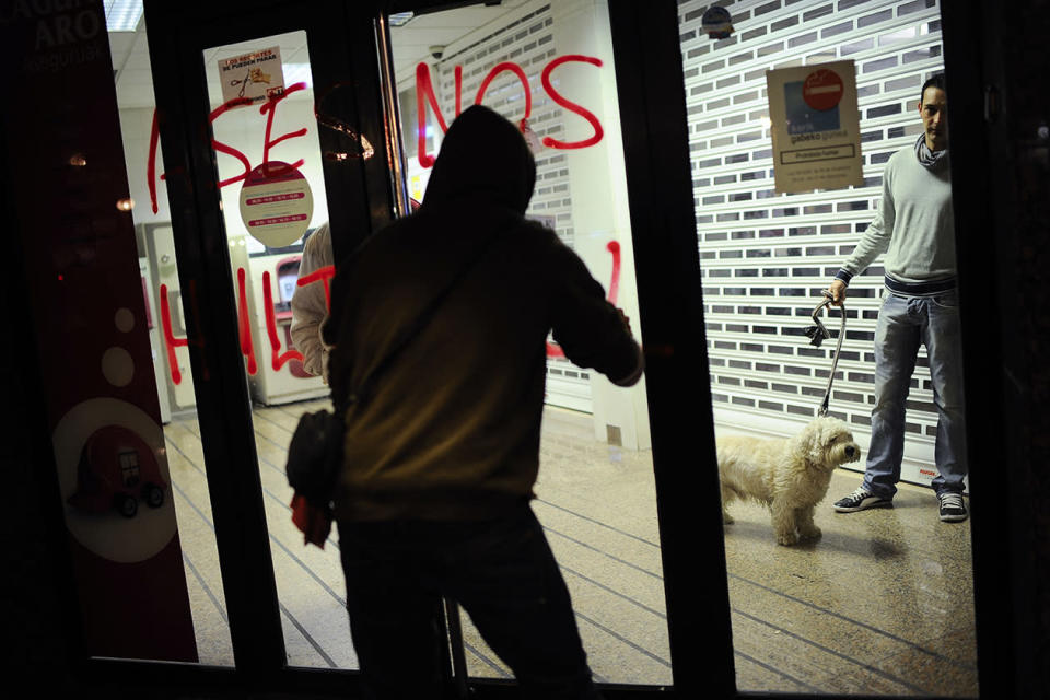 A demonstrator paints a graffiti against banks reading, ''Assassin'' while a man with his dog looks at him , right, from inside a cash dispenser, during a march against evictions, in Barakaldo, northern Spain.