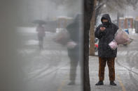 A man wearing a face mask holds a flower bouquet as he stands along a street in Beijing, Friday, Feb. 14, 2020. China on Friday reported another sharp rise in the number of people infected with a new virus, as the death toll neared 1,400. (AP Photo/Mark Schiefelbein)