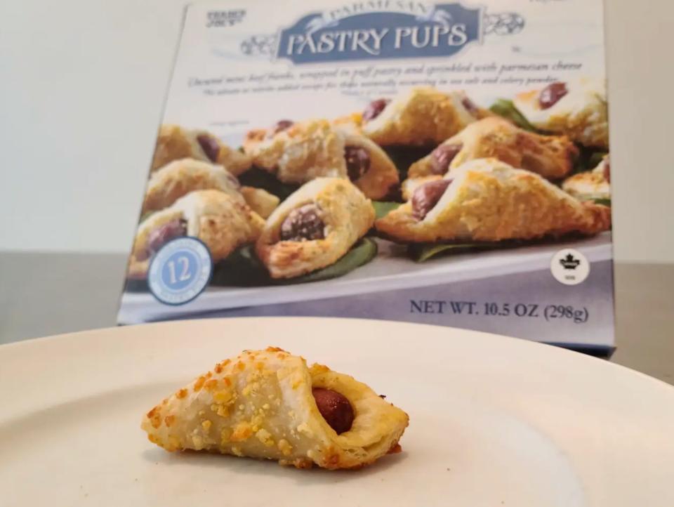 A golden-brown pastry pup on a white plate with a blue box of pastry pups behind it