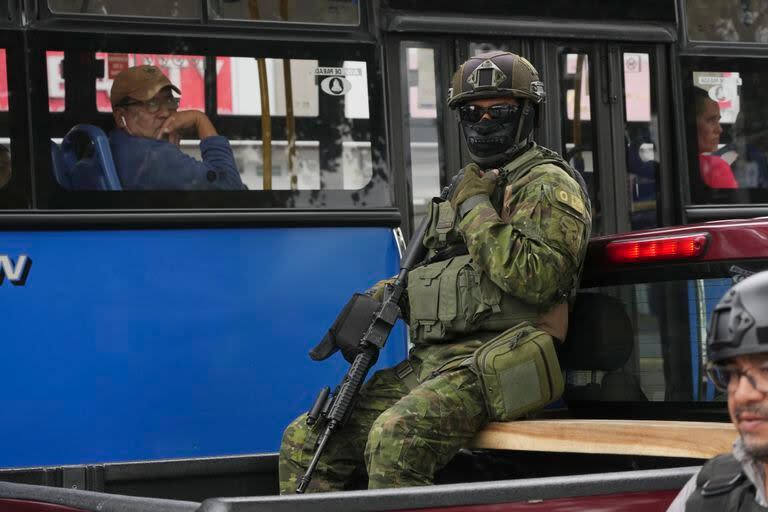 Un soldado se sienta en la parte trasera de un camión mientras patrulla frente a un ómnibus de cercanías en el norte de Quito, Ecuador, el jueves 11 de enero de 2024. (Foto AP/Dolores Ochoa)