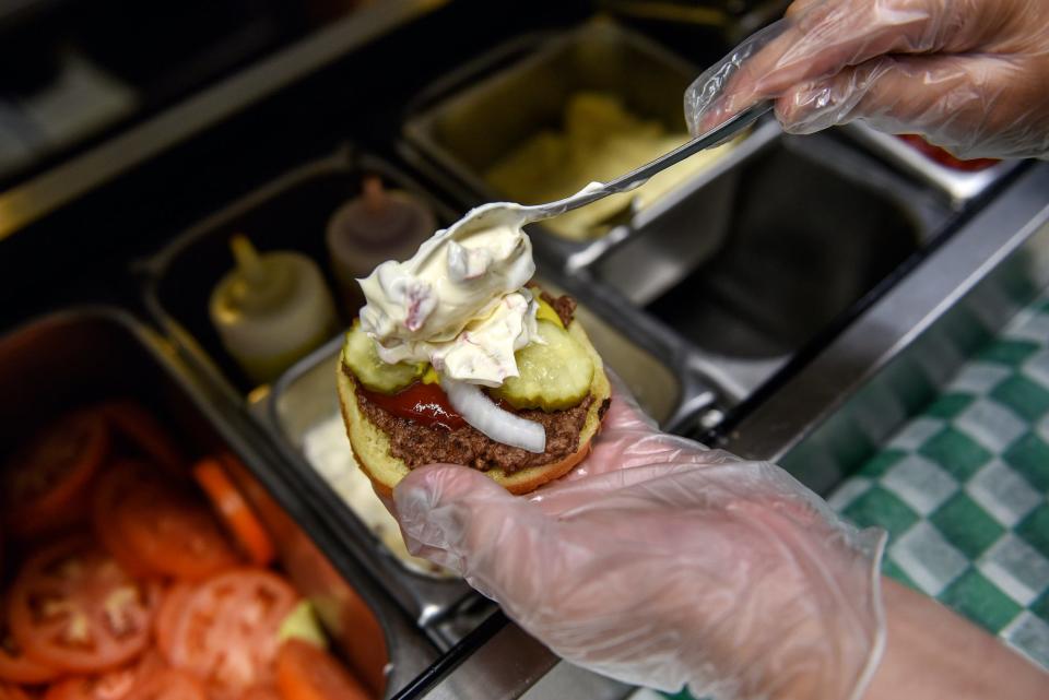 Employee Isabelle Grades puts olive sauce on a burger at Weston's Kewpee Burger on Tuesday, July 16, 2019, in Lansing.