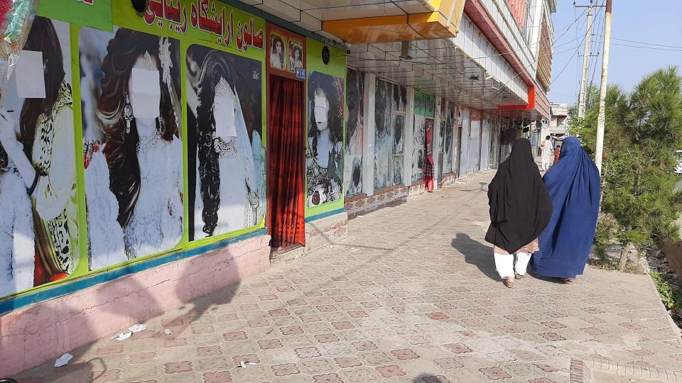 Afghan women walk past large photos of women on the doors of a beauty salons, on which the faces have been obscured amid fear over the ruling Taliban's crackdown on women's rights in the country, in Nangarhar, Afghanistan, September 9, 2021. / Credit: Stringer/Anadolu Agency/Getty