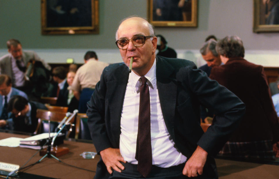 El presidente de la Junta de la Reserva Federal, Paul Volcker, está de pie con las manos en las caderas y fuma un cigarro durante una reunión en Washington, 1982.