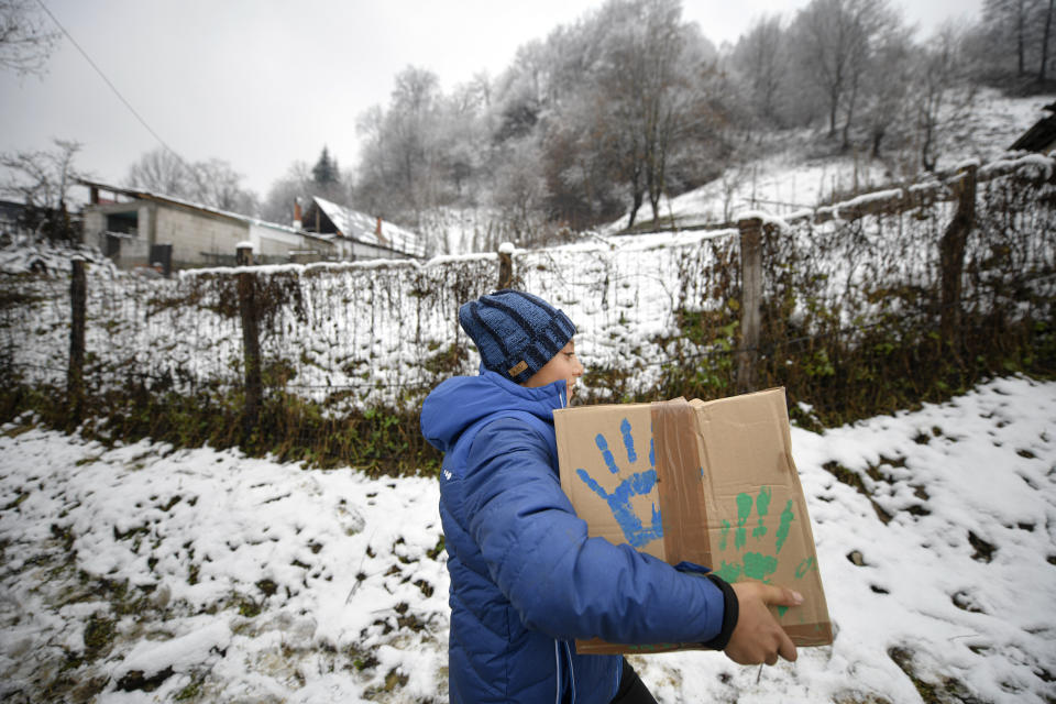 A boy carries a box containing basic food, hygiene and medical products on a muddy slope in Nucsoara, Romania, Saturday, Jan. 9, 2021. Valeriu Nicolae and his team visited villages at the foot of the Carpathian mountains, northwest of Bucharest, to deliver aid. The rights activist has earned praise for his tireless campaign to change for the better the lives of the Balkan country’s poorest and underprivileged residents, particularly the children. The rights activist has earned praise for his tireless campaign to change for the better the lives of the Balkan country’s poorest and underprivileged residents, particularly the children. (AP Photo/Andreea Alexandru)