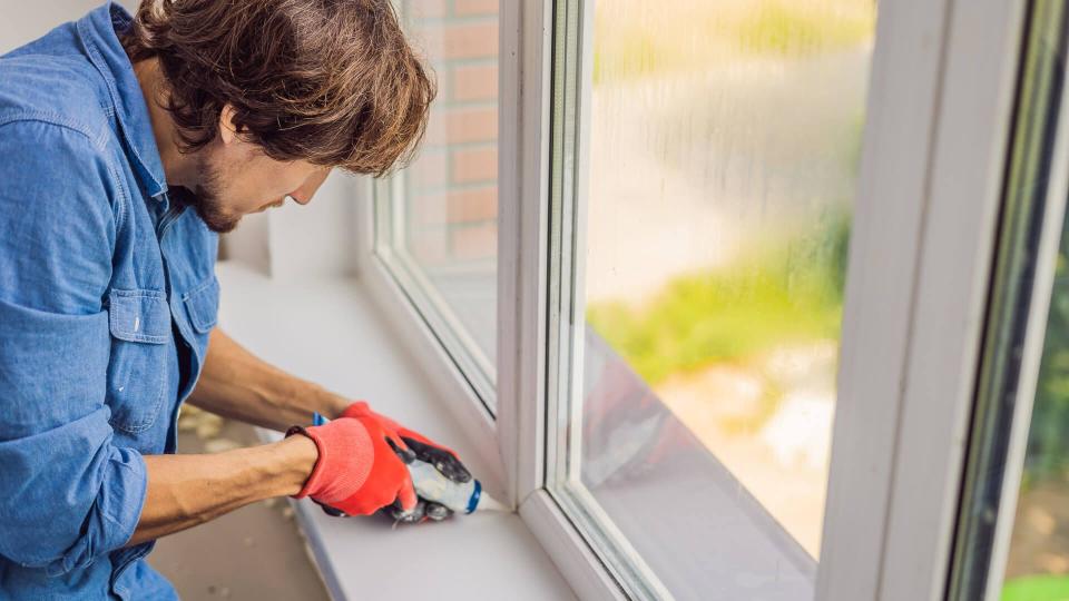 Man in a blue shirt does window installation.