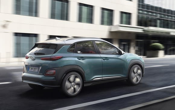 A rear three-quarter view of the Kona Electric as it drives on a city street.