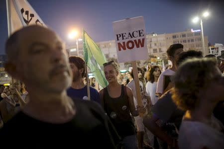 Left-wing protesters, one holding a placard bearing the logo of Peace Now, an Israeli NGO that tracks and opposes Jewish settlement in the occupied West Bank and East Jerusalem, take part in a protest condemning an arson attack in the West Bank, at Rabin square in Tel Aviv, Israel, in this August 1, 2015 file picture. REUTERS/Baz Ratner/Files