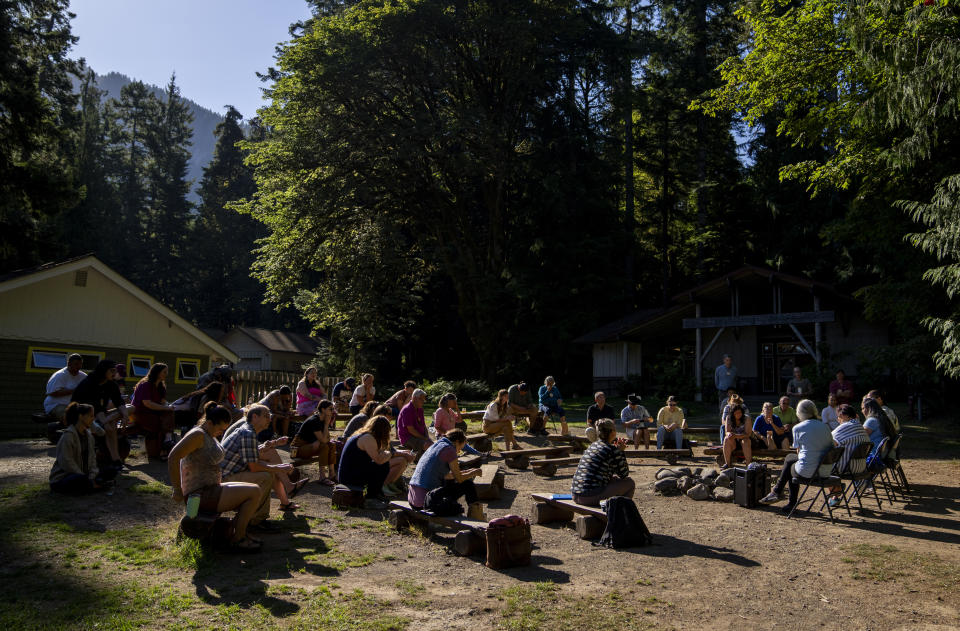 Attendees gather for a morning session on the log benches at NatureBridge in the Olympic National Park during the 2023 Tribal Climate Camp, Thursday, Aug. 17, 2023, near Port Angeles, Wash. Participants representing at least 28 tribes and intertribal organizations gathered to connect and share knowledge as they work to adapt to climate change that disproportionally affects Indigenous communities. More than 70 tribes have taken part in the camps that have been held across the United States since 2016. (AP Photo/Lindsey Wasson)