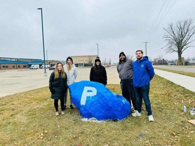 Members of the Perry High School classes of 2014 and 2024 gather around the rock they painted to honor Ahmir Jolliff, who died in the Jan. 4 shootings at the school.