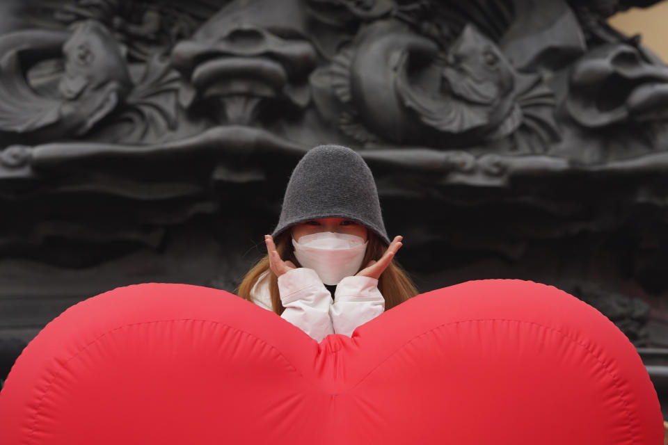 A visitor wearing a mask to protect from the coronavirus poses for photos near a heart shaped balloon displayed at a mall district during the second day of the Chinese Lunar New Year in Beijing on Saturday, Feb. 13, 2021. (AP Photo/Ng Han Guan)