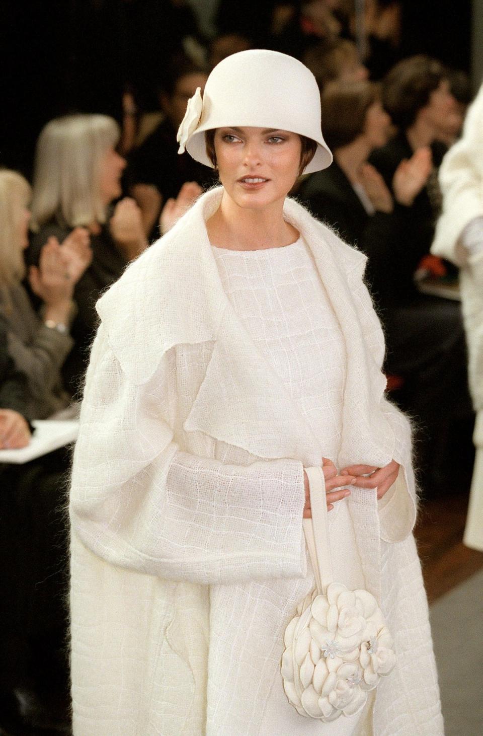 Canadian model Linda Evangelista shows off a white woolen coat withthe traditionnal chanel assorted hat and purse during the presentation of Chanel’s ready-to-wear Fall/Winter 1998/99 collection designed by Karl Lagerfeld 13 March in Paris (AFP via Getty Images)