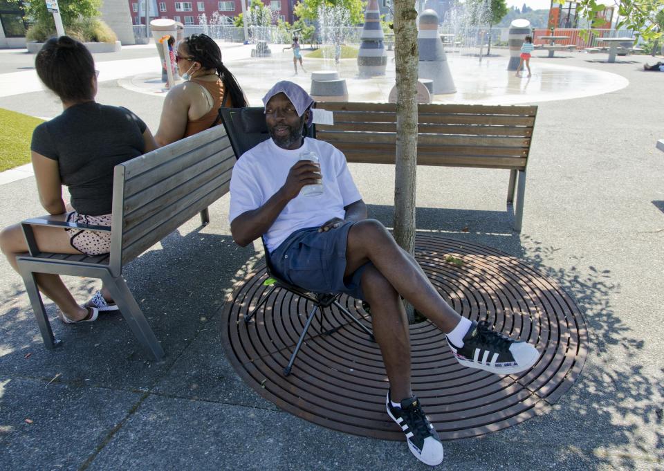 Melvin O'Brien waits in the shade in Yesler Terrace Park while his children play in the spray park during a heat wave hitting the Pacific Northwest, Sunday, June 27, 2021, in Seattle. Yesterday set a record high for the day with more record highs expected today and Monday. (AP Photo/John Froschauer)