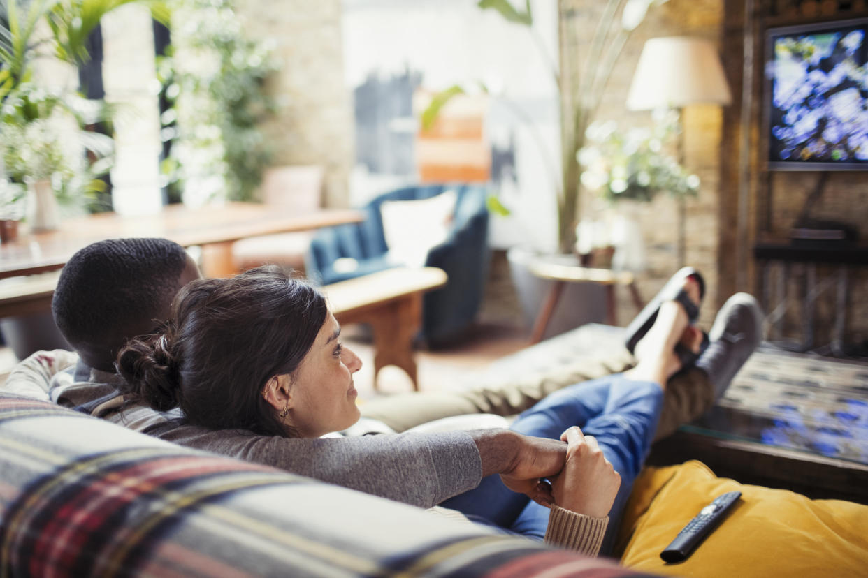 Affectionate young couple watching TV on living room sofa. Photo: Getty