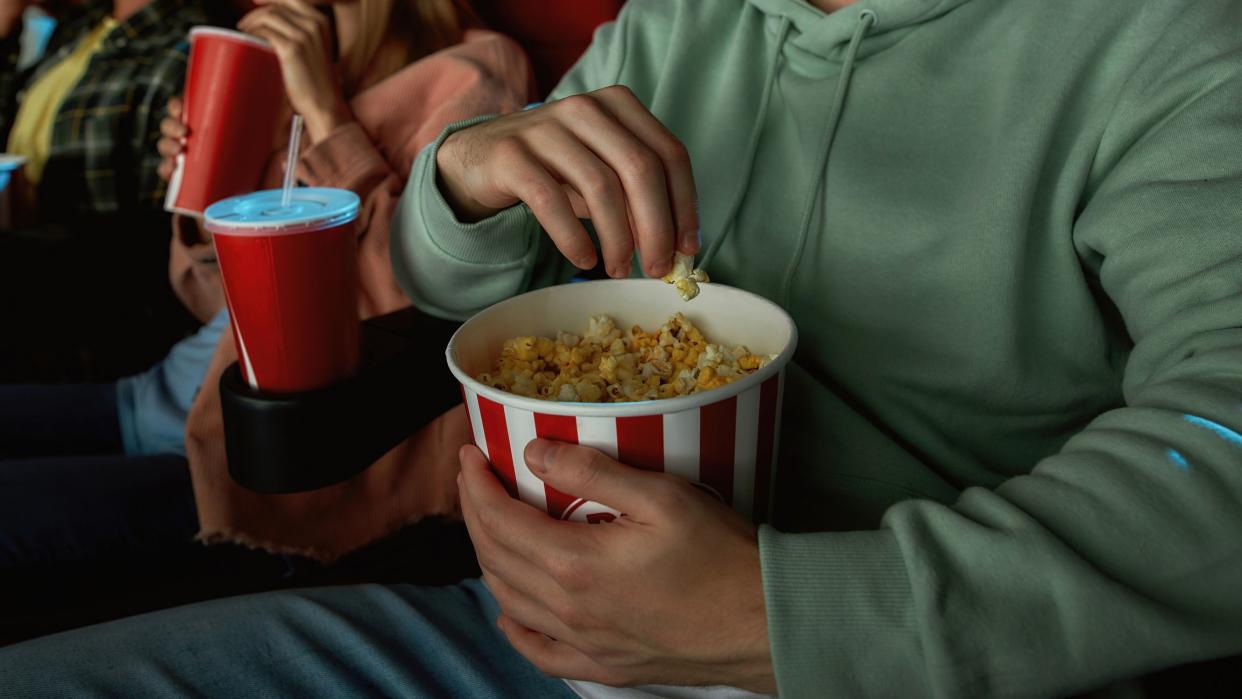 Closeup shot of young guy having popcorn basket while watching movie in cinema auditorium together with friends. Entertainment and people concept. Web Banner